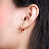 Fine jewellery, silver jewellery plated with rose gold, hypoallergenic, tarnish-free, close-up left view of a Rose gold glazed black hoop earrings worn on a person's ear